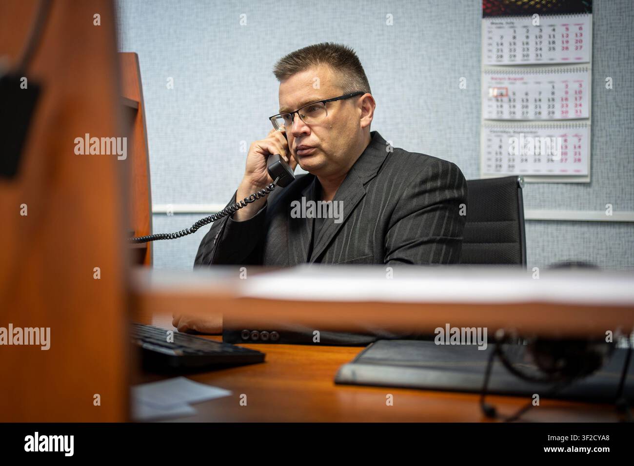 Uomo d'affari serio che parla al telefono fisso mentre lavora alla sua scrivania in ufficio. Comunicazione professionale, trattative commerciali, gestione dell'ufficio Foto Stock