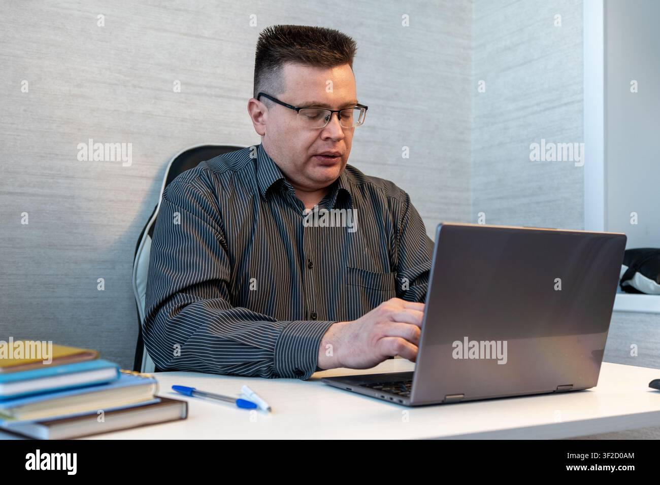 Uomo d'affari stanco che sbadiglia mentre lavora su un laptop in ufficio, alle prese con stanchezza, straordinari, burnout e mancanza di sonno durante una giornata lavorativa impegnativa Foto Stock