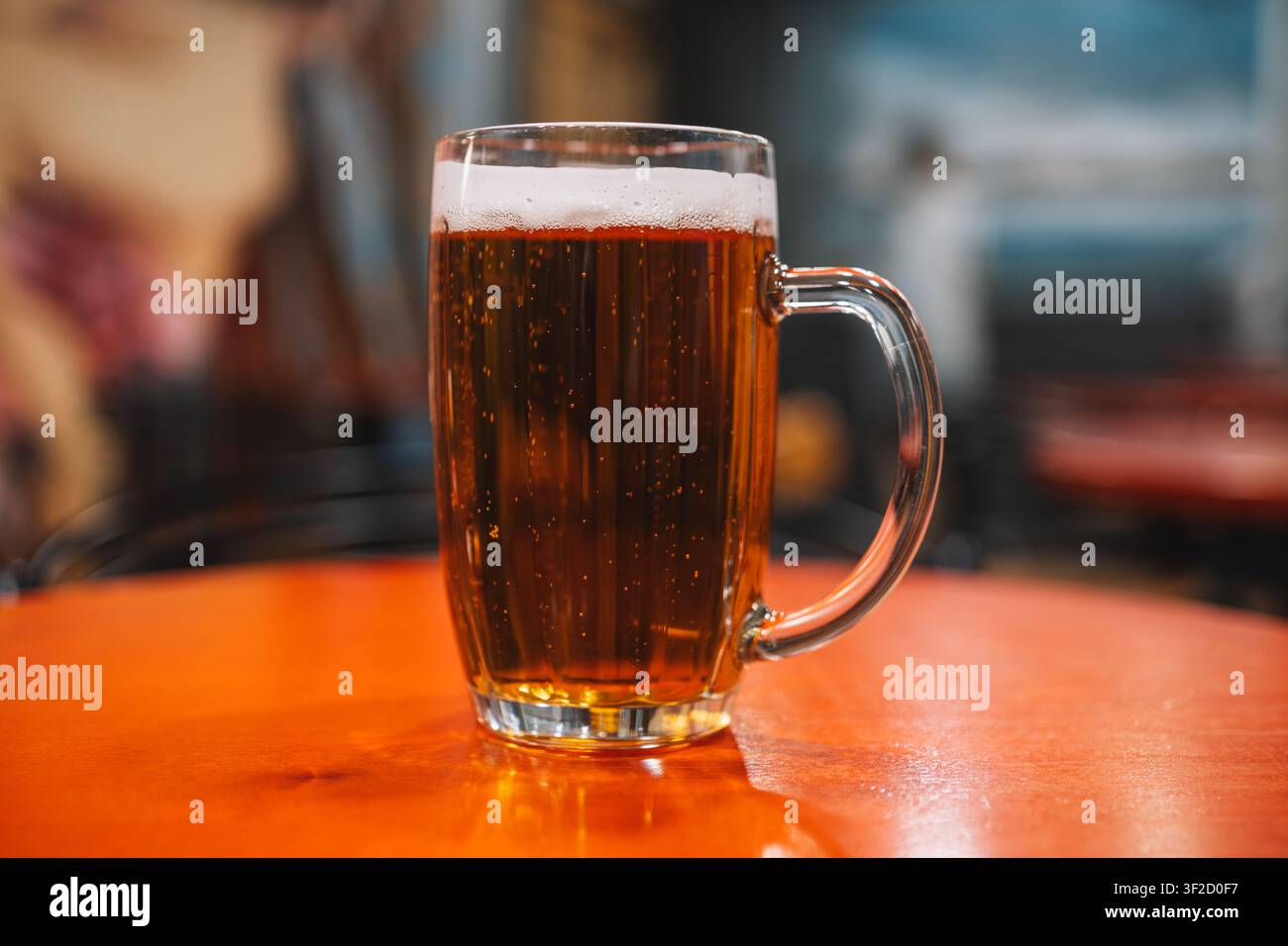 Una tazza di vetro di birra ambrata con una schiuma bianca su un tavolo di legno lucido. Atmosfera da bar, rinfresco freddo e bevanda classica da pub. Foto Stock