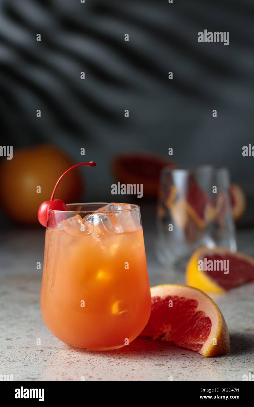Cocktail con ghiaccio e succo di pompelmo. Bere con ghiaccio nel bicchiere congelato e frutta fresca su un tavolo di pietra. Sullo sfondo, le ombre del palmo leav Foto Stock