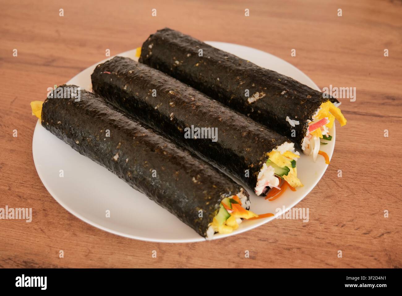 Rotolo di Kimbap fatto in casa su piatto bianco prima del taglio Foto Stock