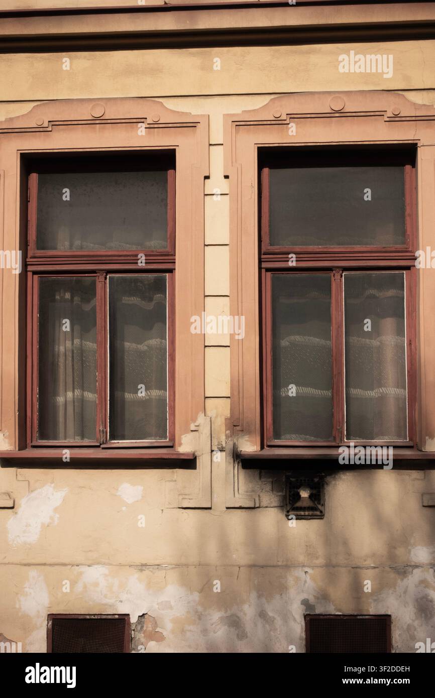Due alte finestre in legno vintage inserite in una facciata beige consumata con intonaco scrostato e decorazioni architettoniche ornamentali Foto Stock