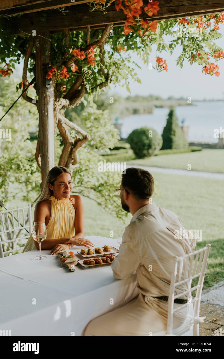 Una coppia condivide una cena deliziosa in una giornata soleggiata in riva al mare, circondata da fiori vivaci e da un paesaggio pittoresco. Foto Stock