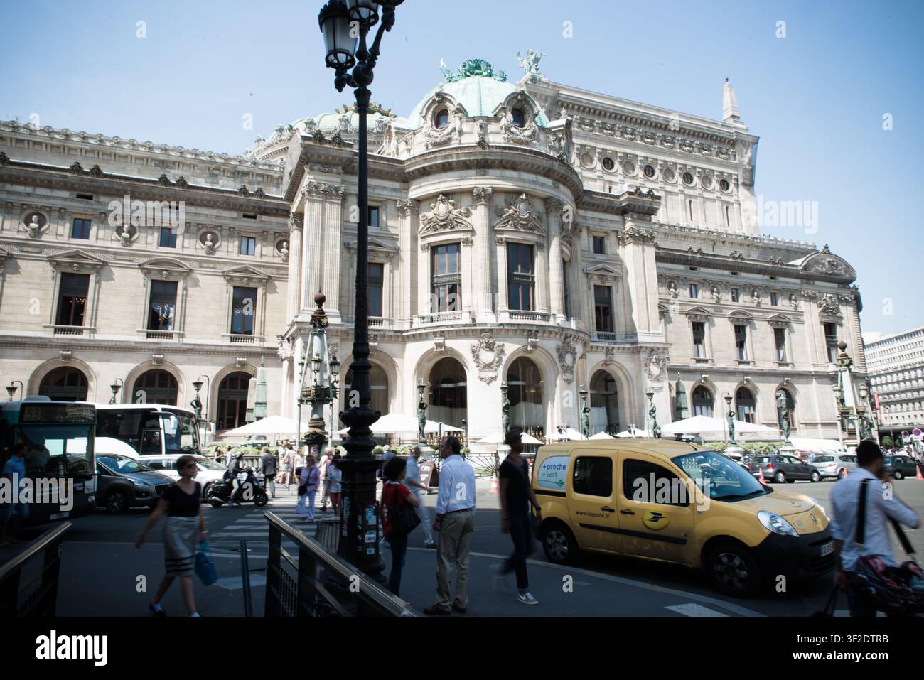 La facciata ornata del Palais Garnier si erge sopra i pedoni e il traffico su una strada cittadina affollata a Parigi, Île-de-France, Francia. Foto Stock