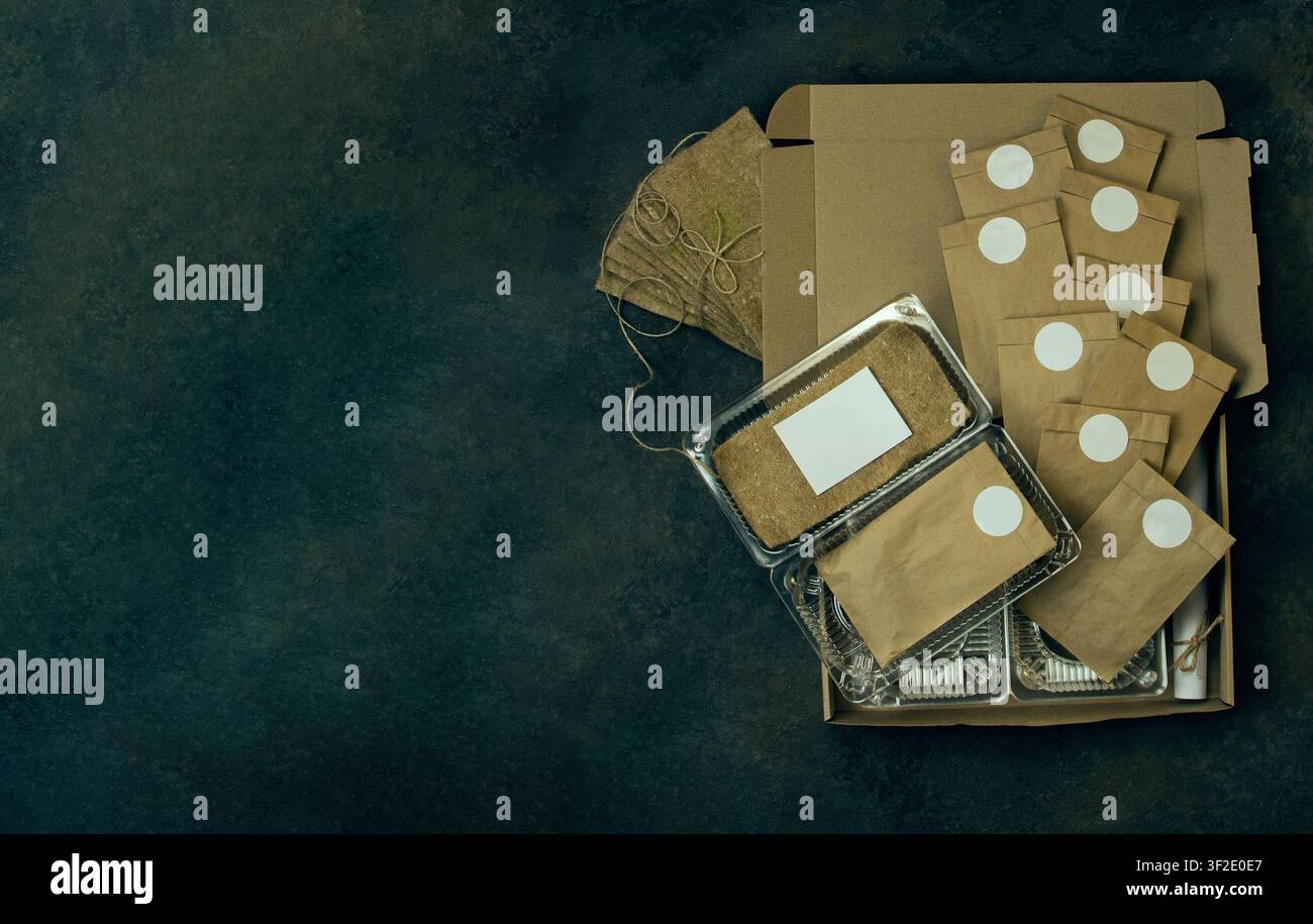 Composizione flat lay presenta un kit per il giardinaggio indoor con materiali ecologici. Sacchetti di carta kraft marrone con adesivi bianchi circolari contengono semi con la scritta Foto Stock