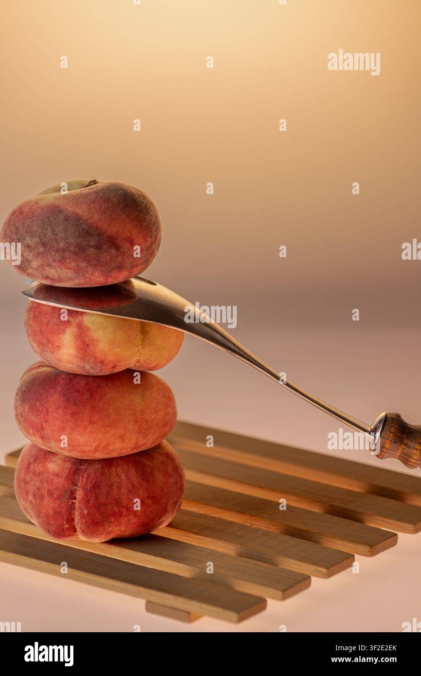 Pesche piatte impilate a forma di torre con un coltello appoggiato accanto su uno sfondo ambrato caldo. Natura morta drammatica da studio con accessorio da cucina, spazio per il testo Foto Stock