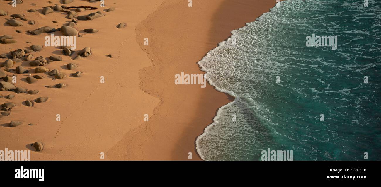 Vista aerea di una spiaggia sabbiosa con rocce sparse e onde turchesi dell'oceano che si infrangono sulla riva. Foto Stock