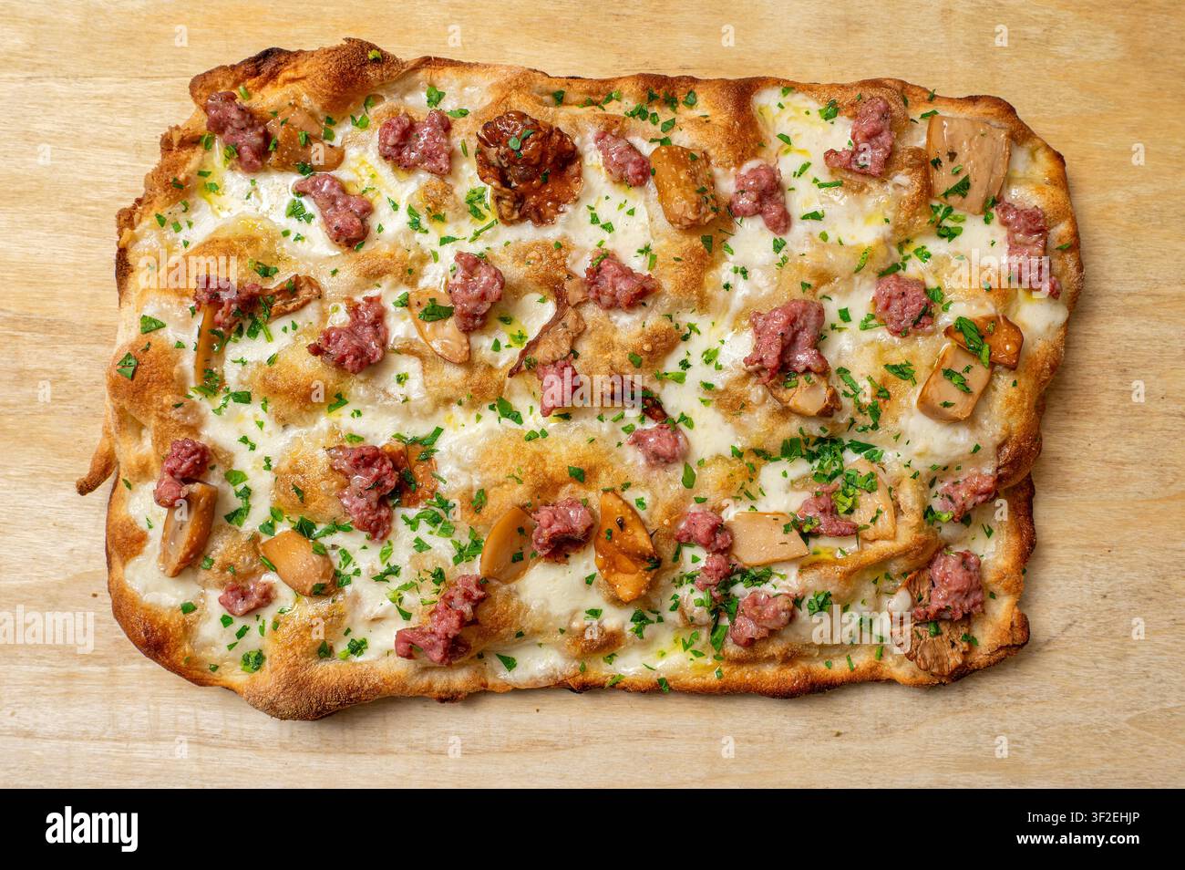 Pinsa romana italiana ricoperta di salsiccia, funghi porcini, mozzarella fusa e prezzemolo fresco, presentata su una tavola di legno Foto Stock