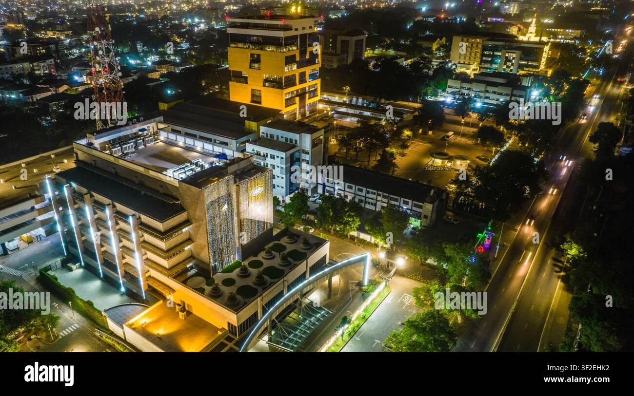Vista aerea di un moderno complesso di edifici per uffici illuminato di notte con scie di luce del traffico sulla strada adiacente in Ghana. Foto Stock