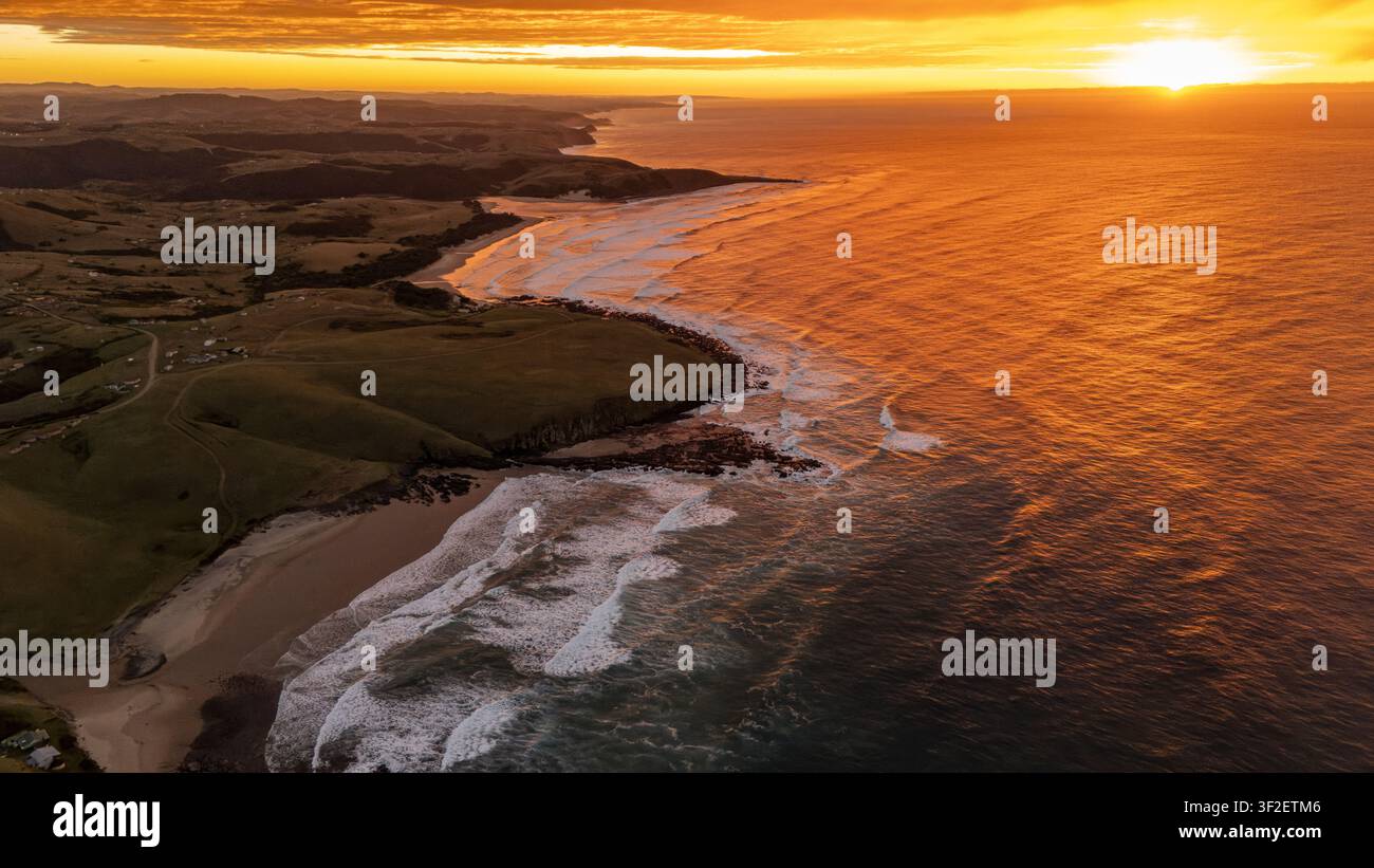 Vista aerea con drone di uno spettacolare sorgere dorato che illumina la costa selvaggia e frastagliata del Capo Orientale, in Sudafrica. Dolci colline verdi, Foto Stock