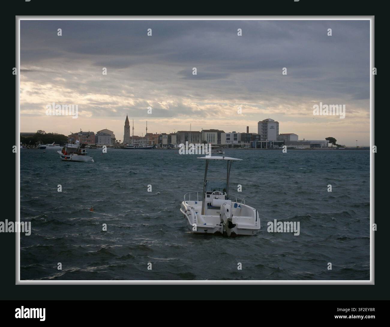 Mare, città, moto ondoso, nuvole grigie, mare agitato, piccola barca Foto Stock