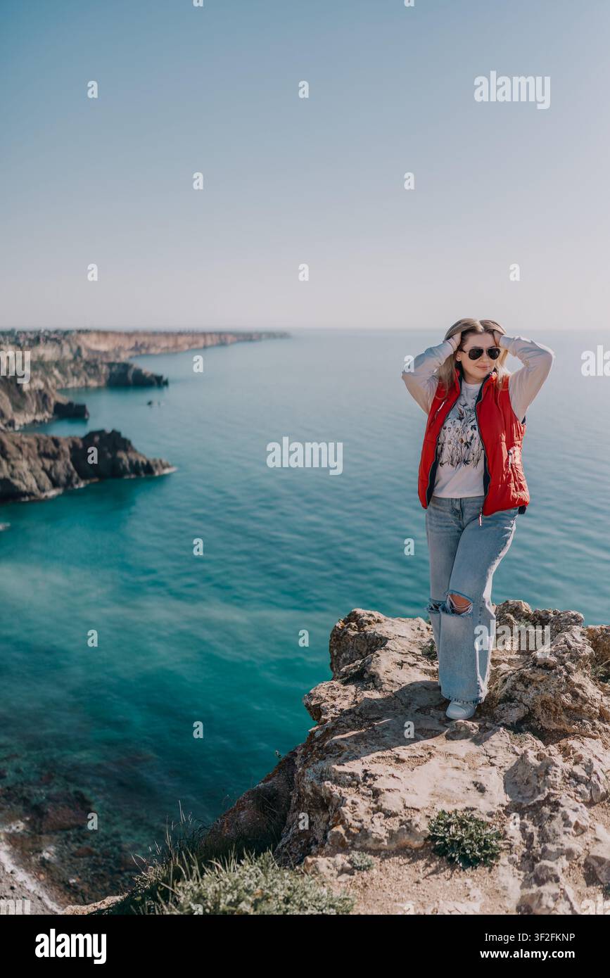 Viaggiatrice sulla costa dell'oceano, giovane donna in piedi su una scogliera rocciosa che si affaccia sul mare turchese, godendosi una vista panoramica sulla costa Foto Stock
