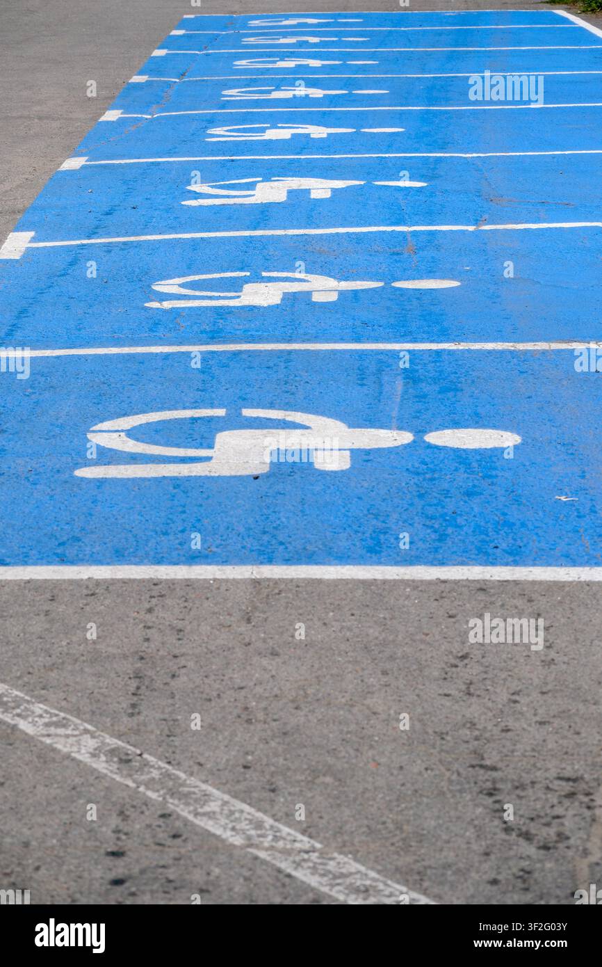 Posti parcheggio accessibili blu segnalati con simboli di sedia a rotelle in un'area di parcheggio pubblica. Posti parcheggio riservati ai disabili che rappresentano l'accessibilità, i Foto Stock