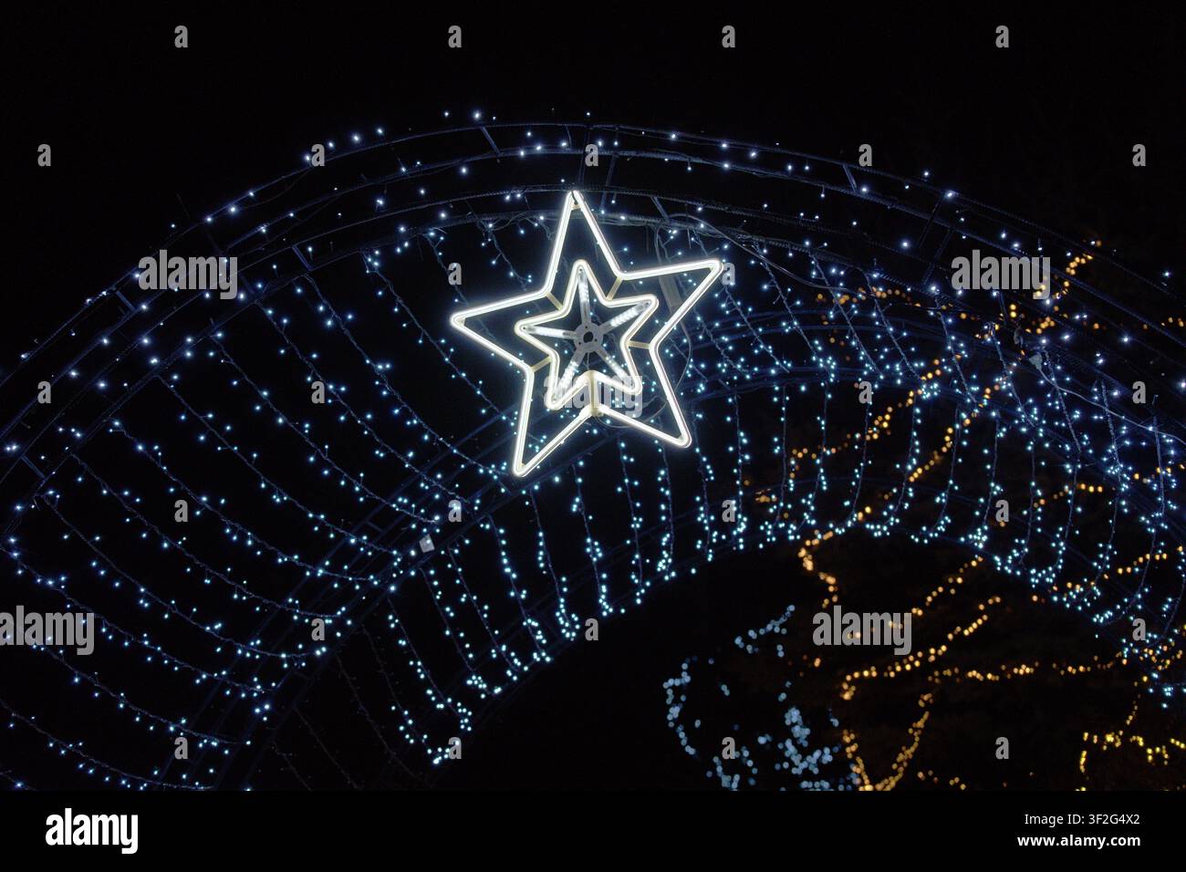 stella illuminata brilla vivacemente nelle decorazioni festive per le vacanze di notte, adornata con luci a filo e accenti metallici, vista grandangolare, bianco an Foto Stock