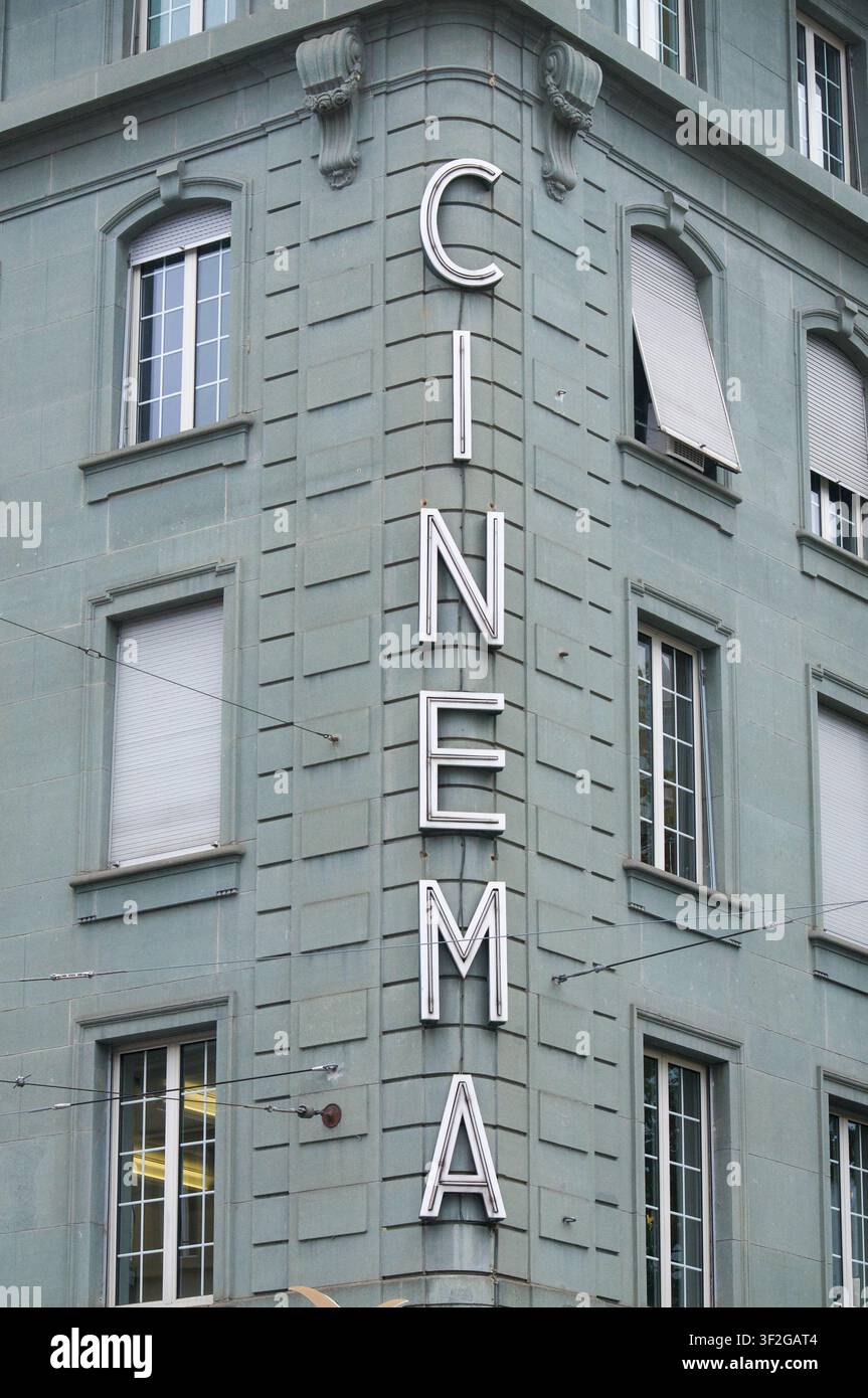 Insegna al neon verticale vintage con la scritta CINEMA montata sull'angolo di una classica facciata edificio grigio-blu. La struttura architettonica presenta simmetria Foto Stock