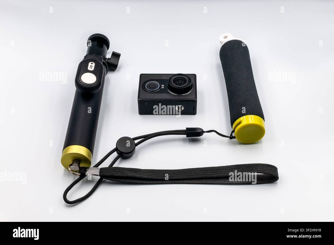Una fotocamera d'azione nera circondata da accessori, tra cui un bastone selfie con telecomando e una maniglia galleggiante su uno sfondo bianco senza cuciture Foto Stock