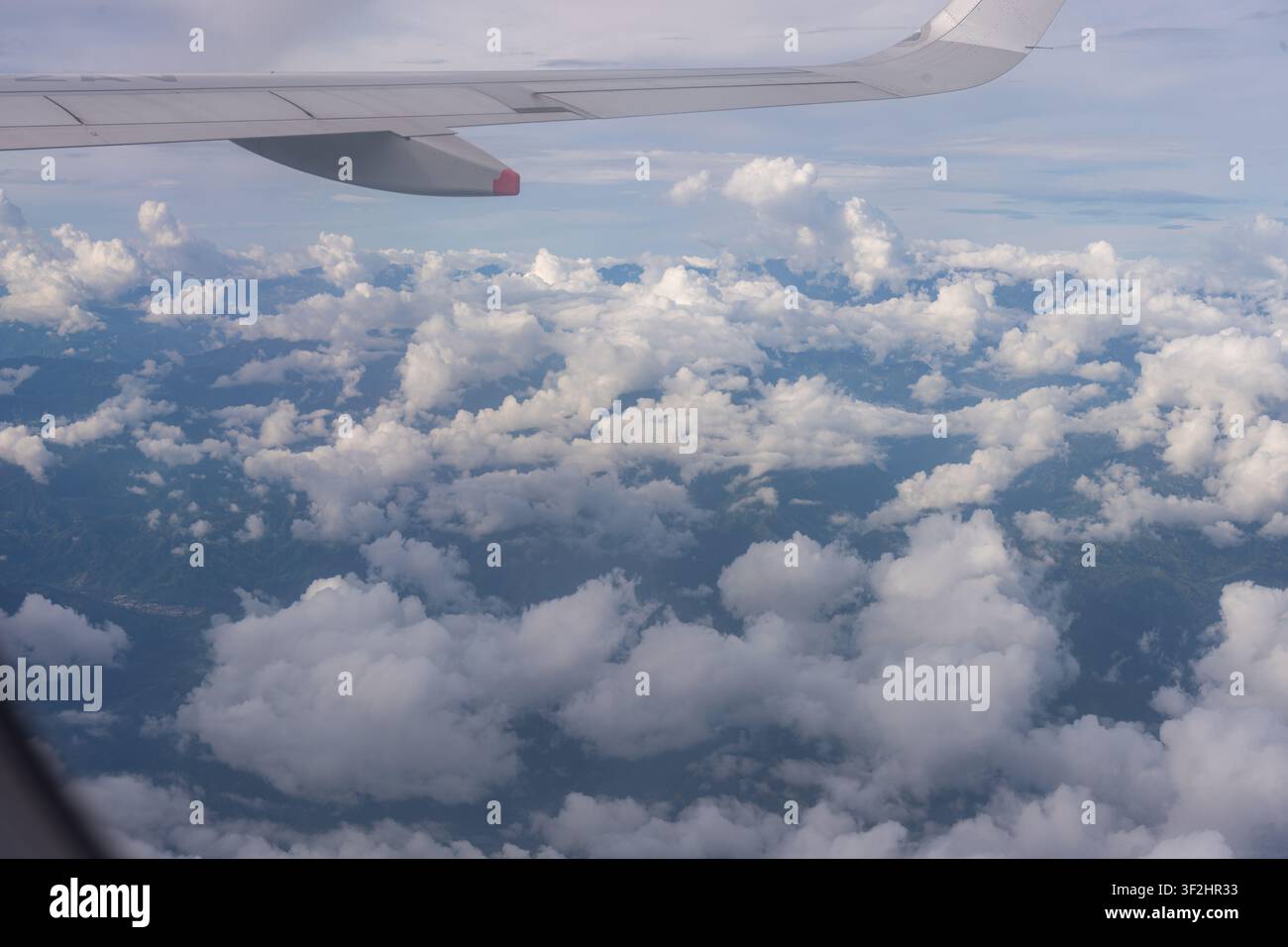 Ala di aereo che scivola sopra una vasta distesa di soffici nuvole bianche cumulus, osservando la superficie terrestre attraverso le aperture nelle nuvole durante un internato Foto Stock