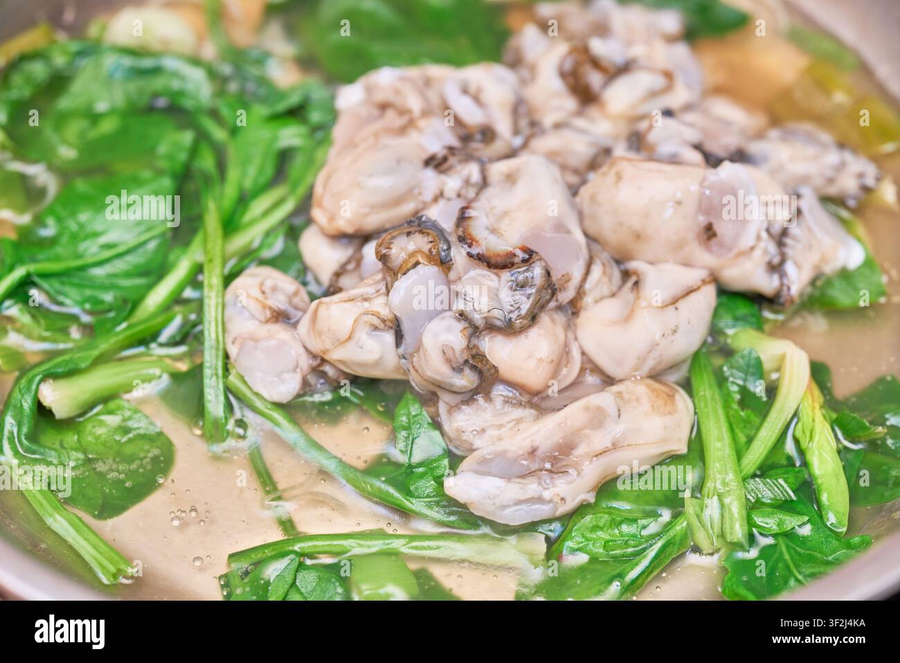 Frittelle di ostriche e spinaci che cuociono in pentola, un classico comfort food invernale stagionale. Perfetto per editoriali culinari e siti di ricette. Foto Stock