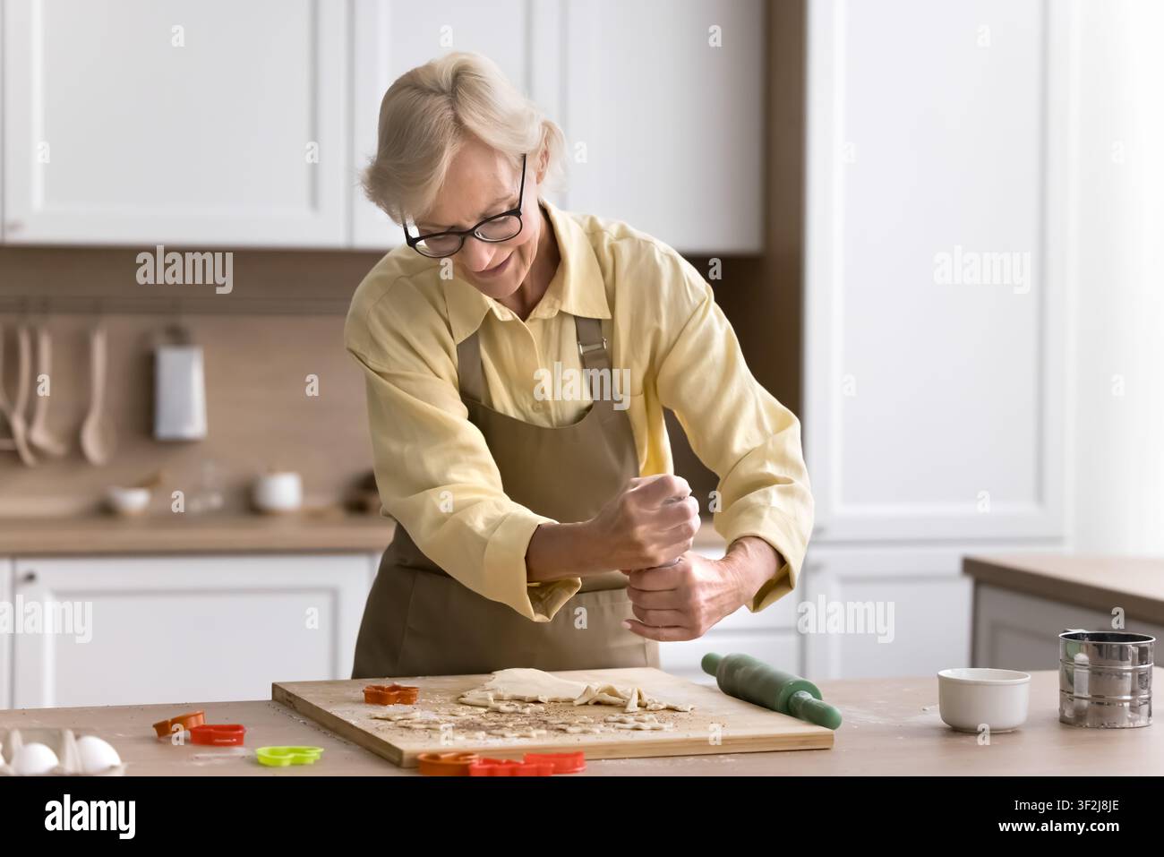 Anziana che spolvera cannella sulla pasta, cucina biscotti in cucina Foto Stock
