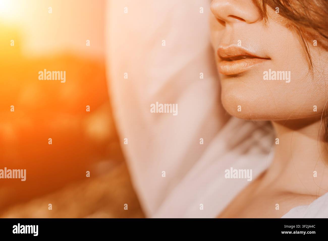 Labbra di donna all'alba, riposanti in morbida biancheria da letto di lino bianco durante la calda luce dorata dell'ora del mattino per una mattina serena Foto Stock