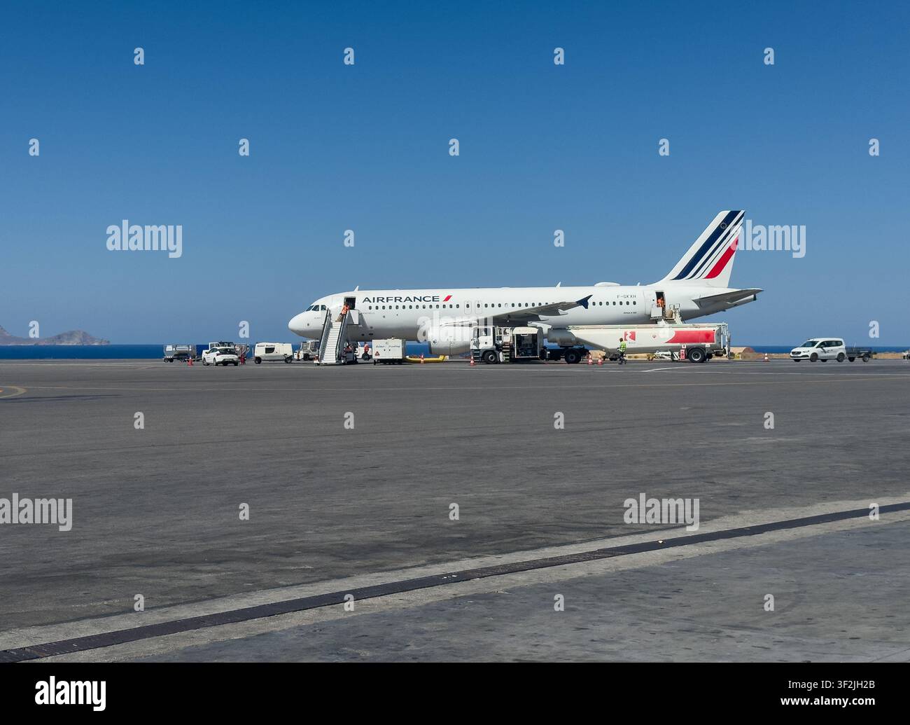 Air France Airbus A320 parcheggiato sulla pista mentre riceve servizi di handling a terra e rifornimento sotto un cielo blu sereno. Foto Stock