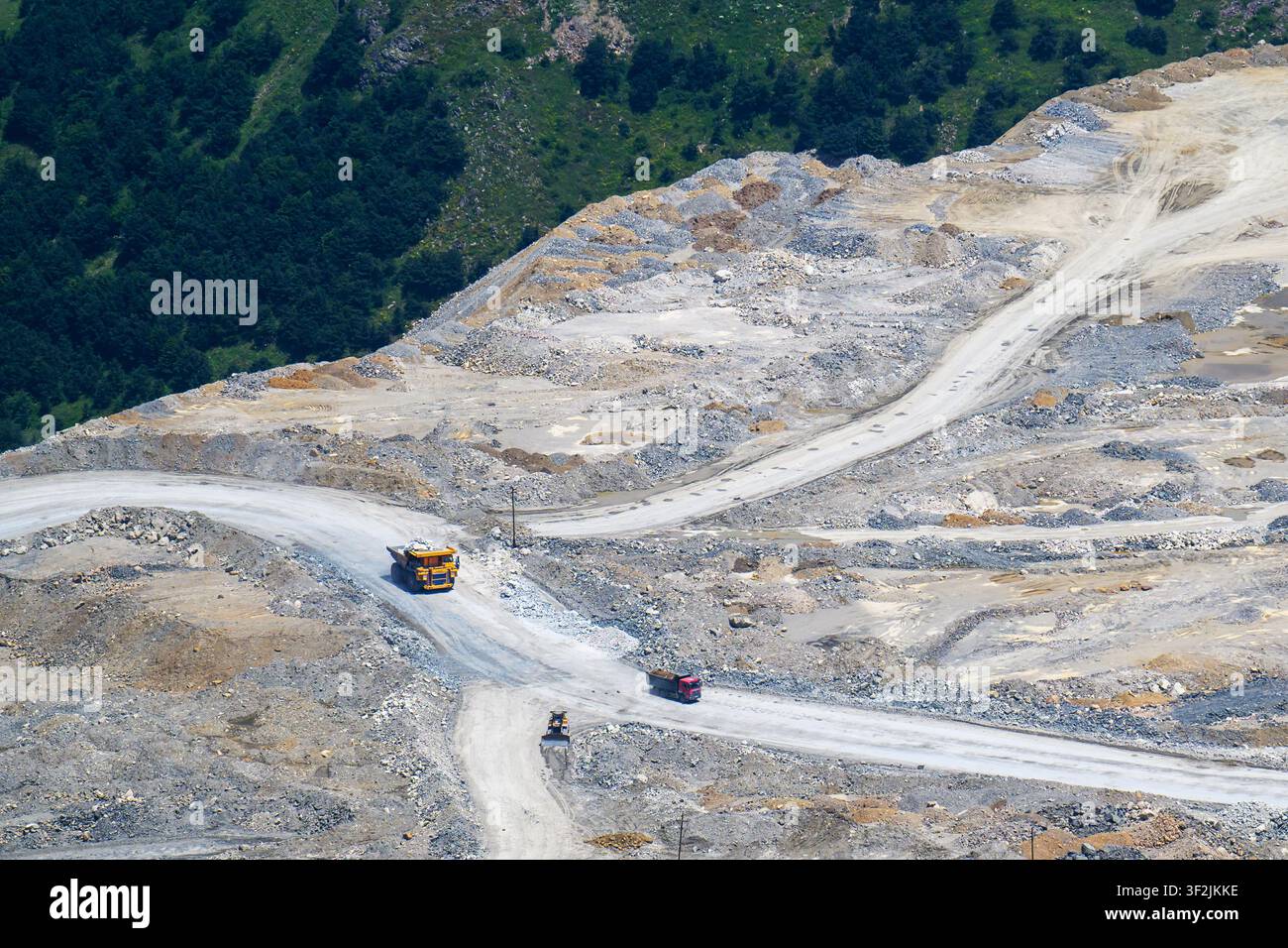 Vista aerea di una cava con macchinari pesanti su strade sterrate. Terreno roccioso e colline verdi circondano il sito. Non sono visibili animali o piante Foto Stock