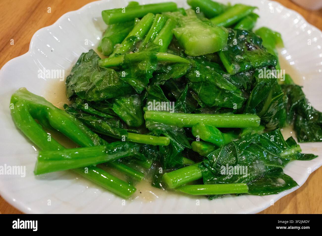Un piatto di broccolo cinese vivace e lucido, saltato in padella e luccicante con una salsa all'aglio saporita, pronto per essere gustato come contorno fresco. Foto Stock