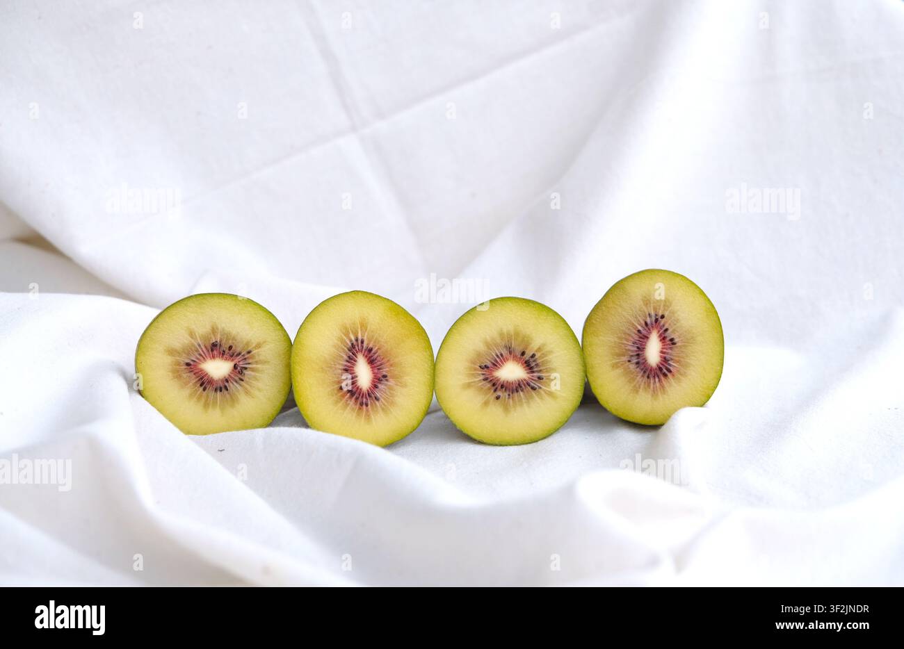 Metà del kiwi rosso su uno sfondo tessile di colore chiaro. Foto Stock