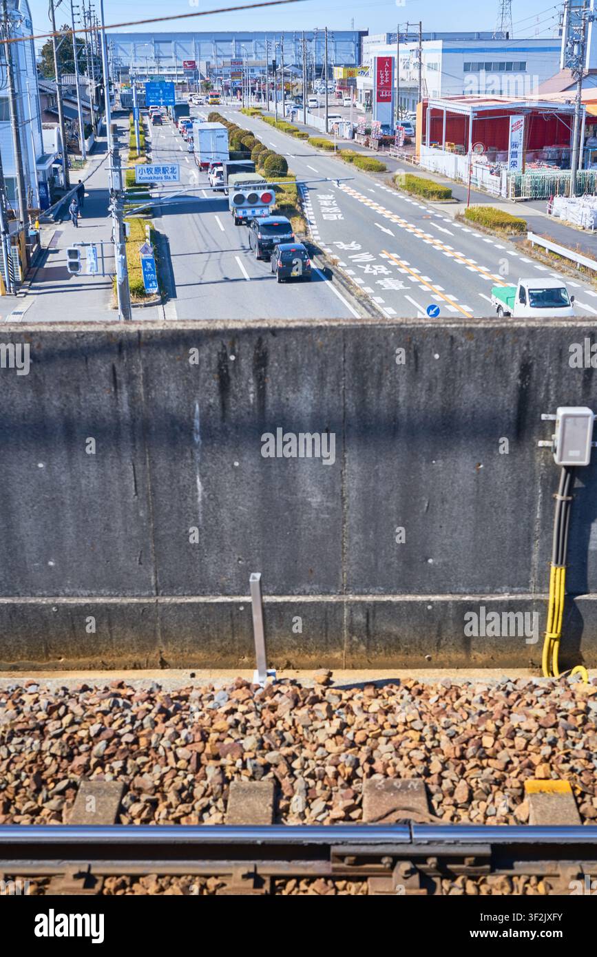 Vista di un binario ferroviario sopraelevato che si affaccia su una strada suburbana trafficata e una barriera in cemento, perfetta per gli editoriali sull'infrastruttura urbana giapponese Foto Stock