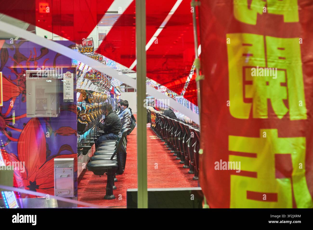 Clienti che giocano a macchinette pachinko illuminate in un vivace arcade giapponese, perfetto per gli editoriali sulle destinazioni di viaggio e i blog culturali Foto Stock