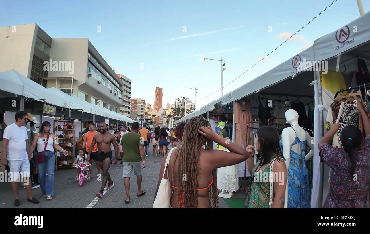 SALVADOR, BRASILE - 10 MARZO 2026: Turisti e locali sfogliano vari stand di abbigliamento e souvenir in un mercato di strada all'aperto sotto tende bianche a Salv Foto Stock