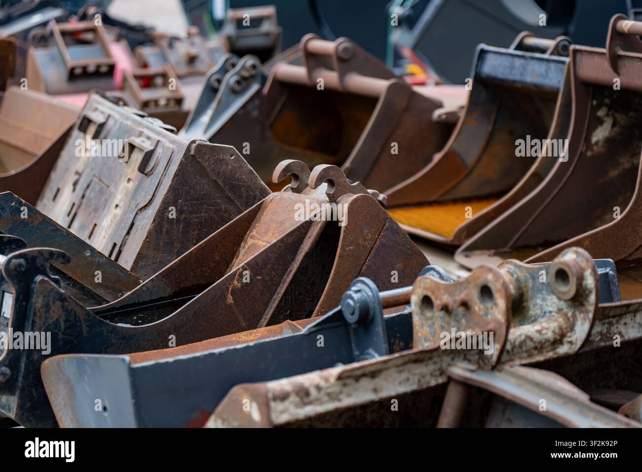 Accessori di scavo in acciaio arrugginito per trattori movimento terra disposti in fila che simboleggiano l'ingegneria metallica e le operazioni industriali Foto Stock