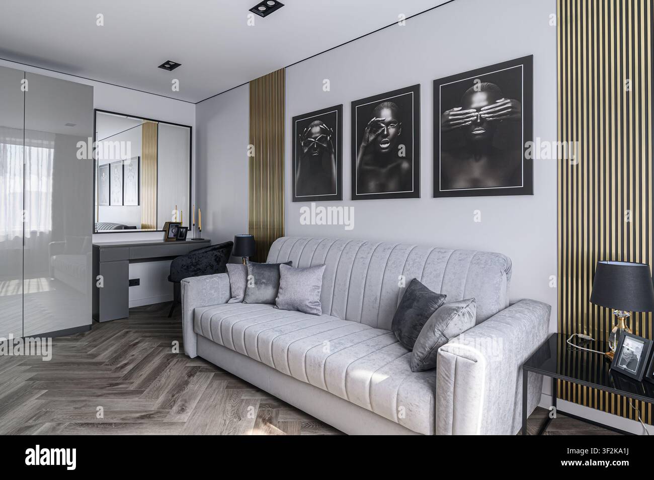 Soggiorno moderno con divano grigio, ritratti in bianco e nero, dettagli dorati e pavimentazione in parquet. Design d'interni chic, contemporaneo ed elegante Foto Stock