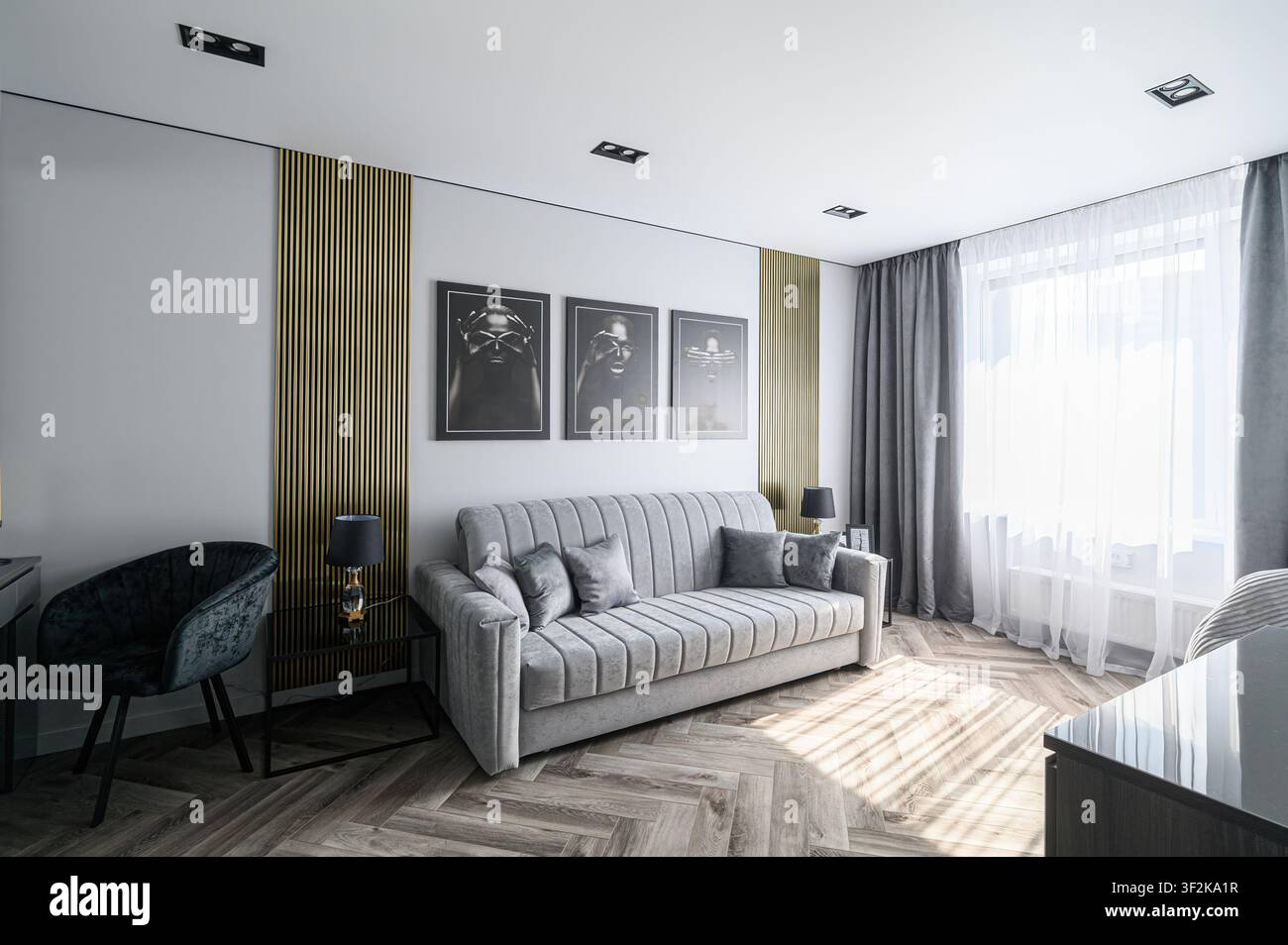 Soggiorno elegante con un divano grigio, opere d'arte in bianco e nero e dettagli in legno. La luce del sole filtra attraverso la finestra Foto Stock