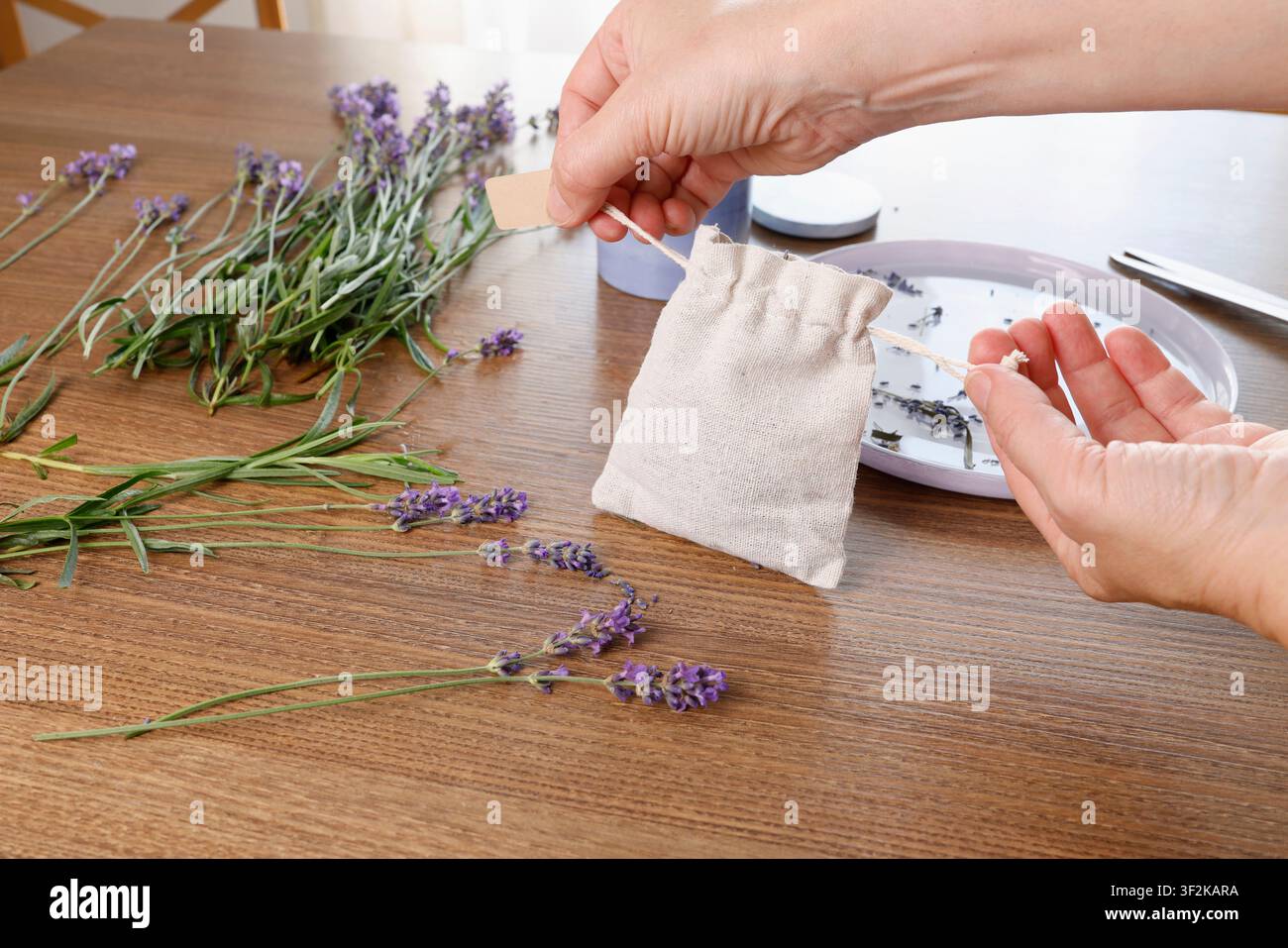 Mani che legano una borsa di lino naturale con cordoncino per impacchettare un sacchetto di lavanda su un tavolo di legno con fiori botanici freschi per piccoli oggetti fatti a mano creativi Foto Stock