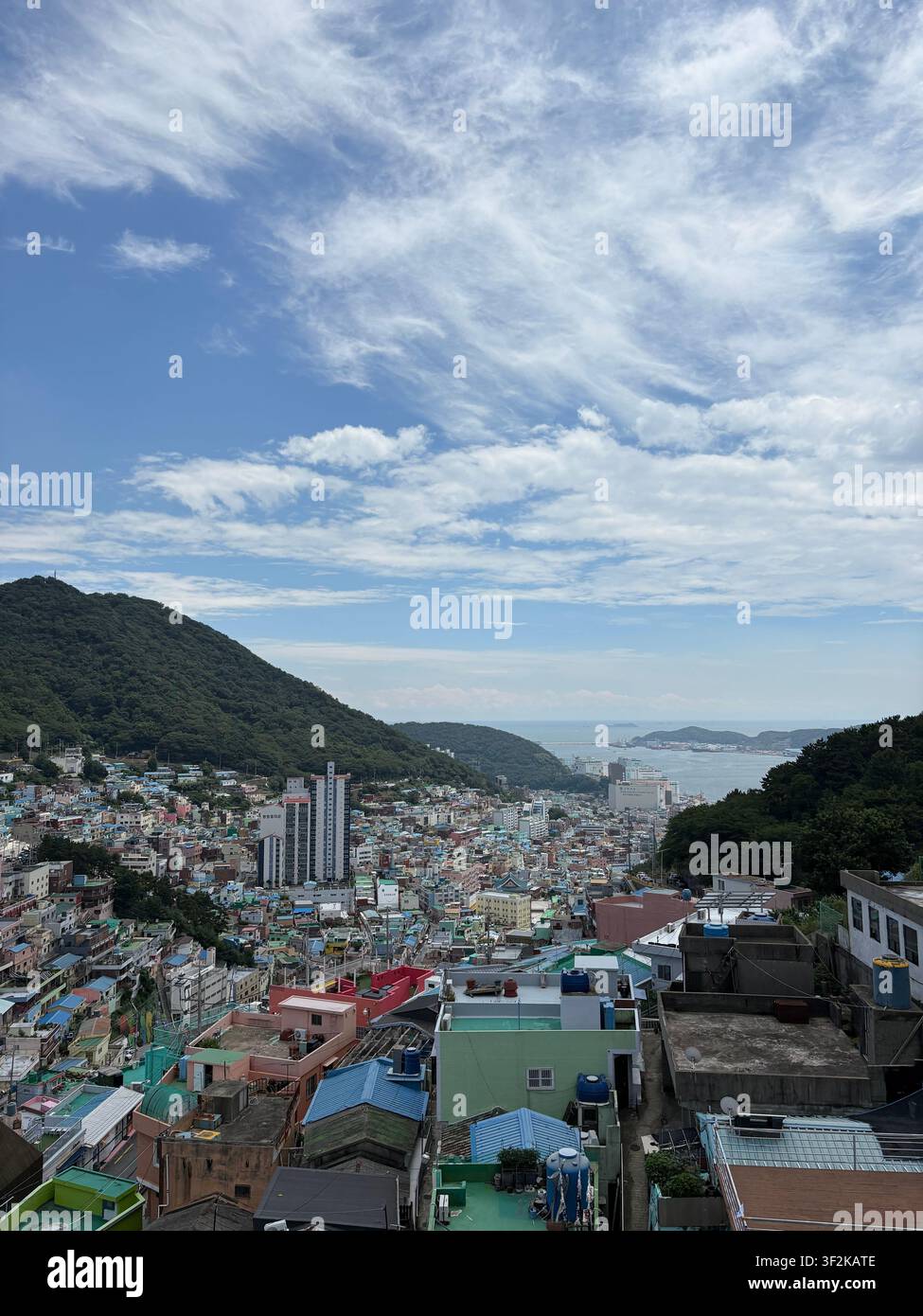 Vista aerea del villaggio culturale di Gamcheon con case colorate a cascata che scendono lungo il pendio verso la baia di Busan, in Corea del Sud, sotto un cielo nuvoloso drammatico Foto Stock