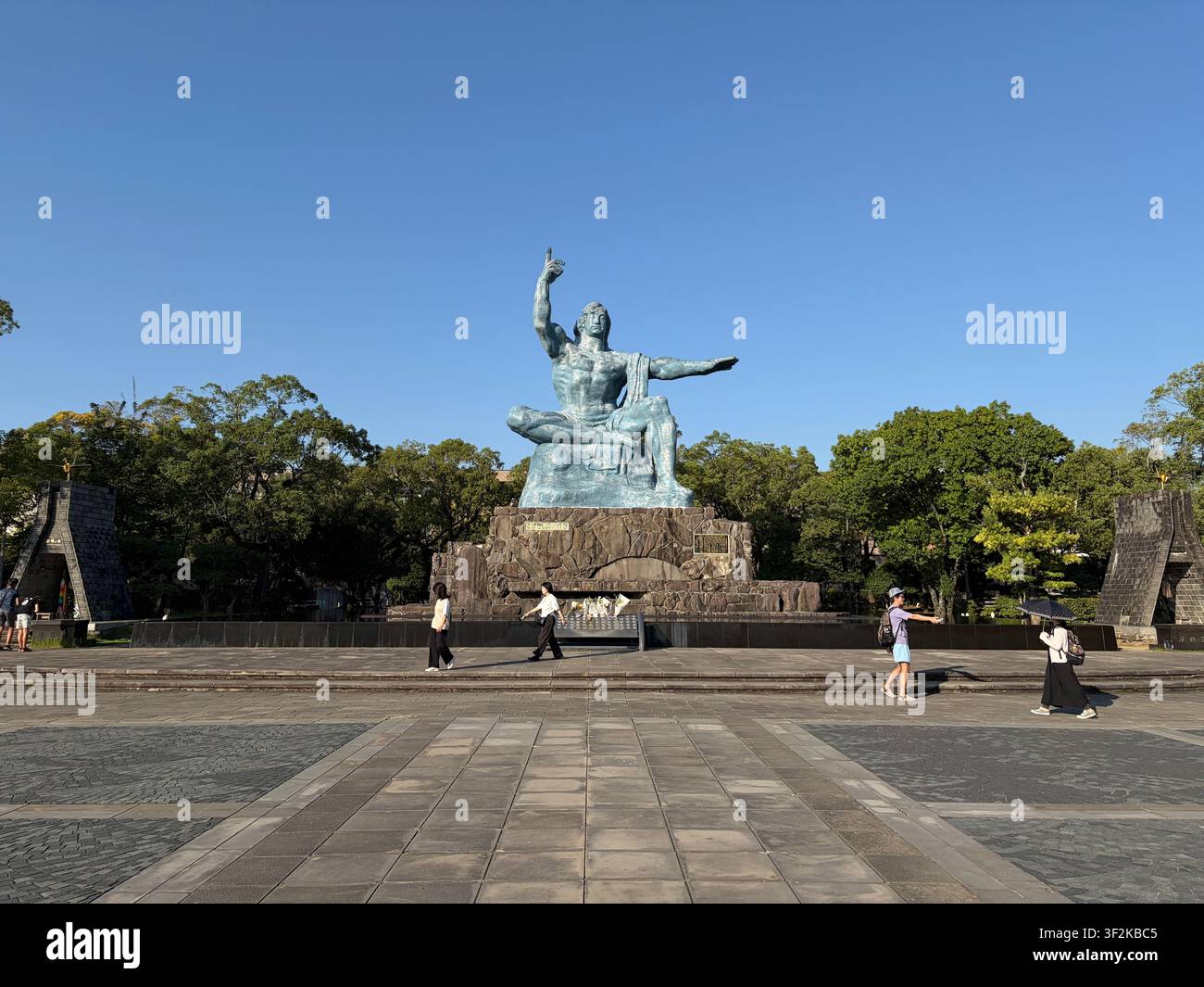 12 ottobre 2025, Nagasaki, Giappone – Statua della Pace in bronzo di Seibo Kitamura al Parco della Pace di Nagasaki, sito commemorativo della bomba atomica, con visitatori sotto un cielo blu terso. - Immagine stock catturata con smartphone