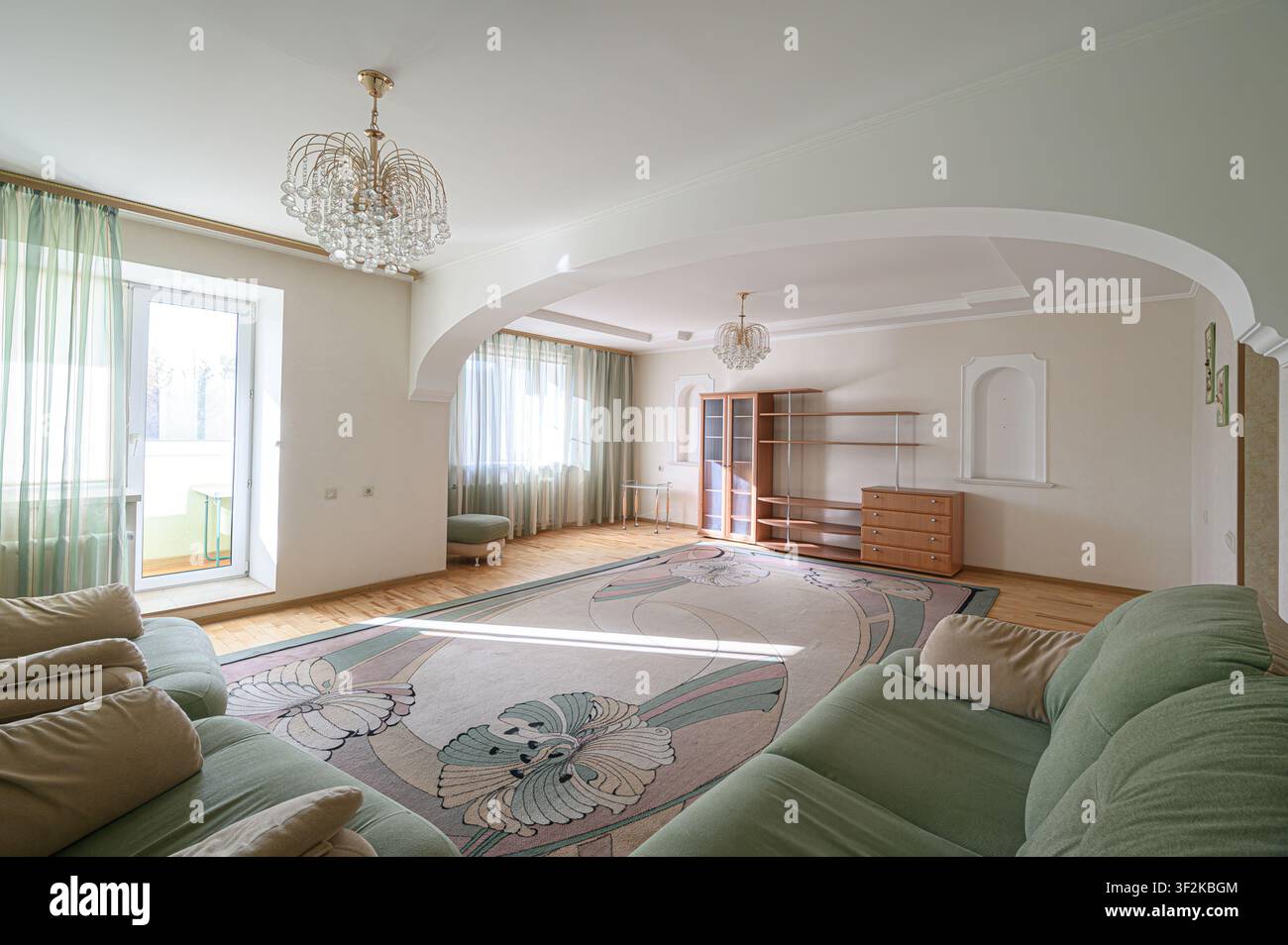 ampio soggiorno con un morbido divano verde, porta ad arco e elegante lampadario di cristallo Foto Stock