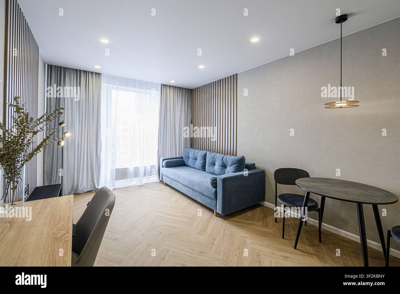 Spazio abitativo accogliente con un divano blu, dettagli in legno e una moderna apparecchiatura da tavolo. Atmosfera luminosa e ariosa Foto Stock
