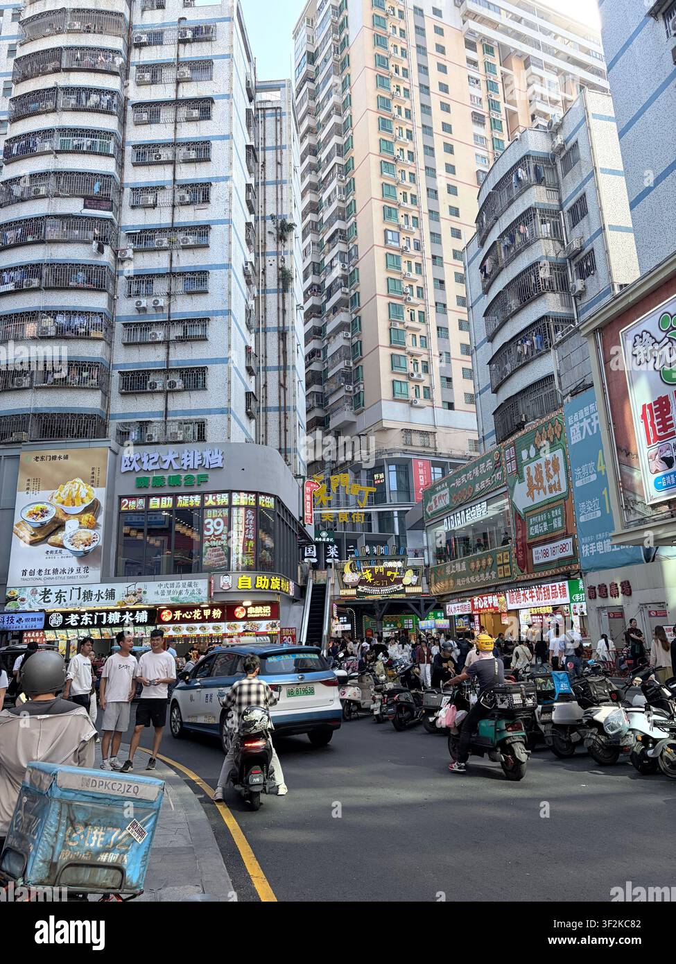 25 ottobre 2025, distretto di Luohu, Shenzhen, Cina – Scena urbana densa di strada con cartelli commerciali cinesi colorati, grattacieli, pedoni e motociclette. - Immagine stock catturata con smartphone
