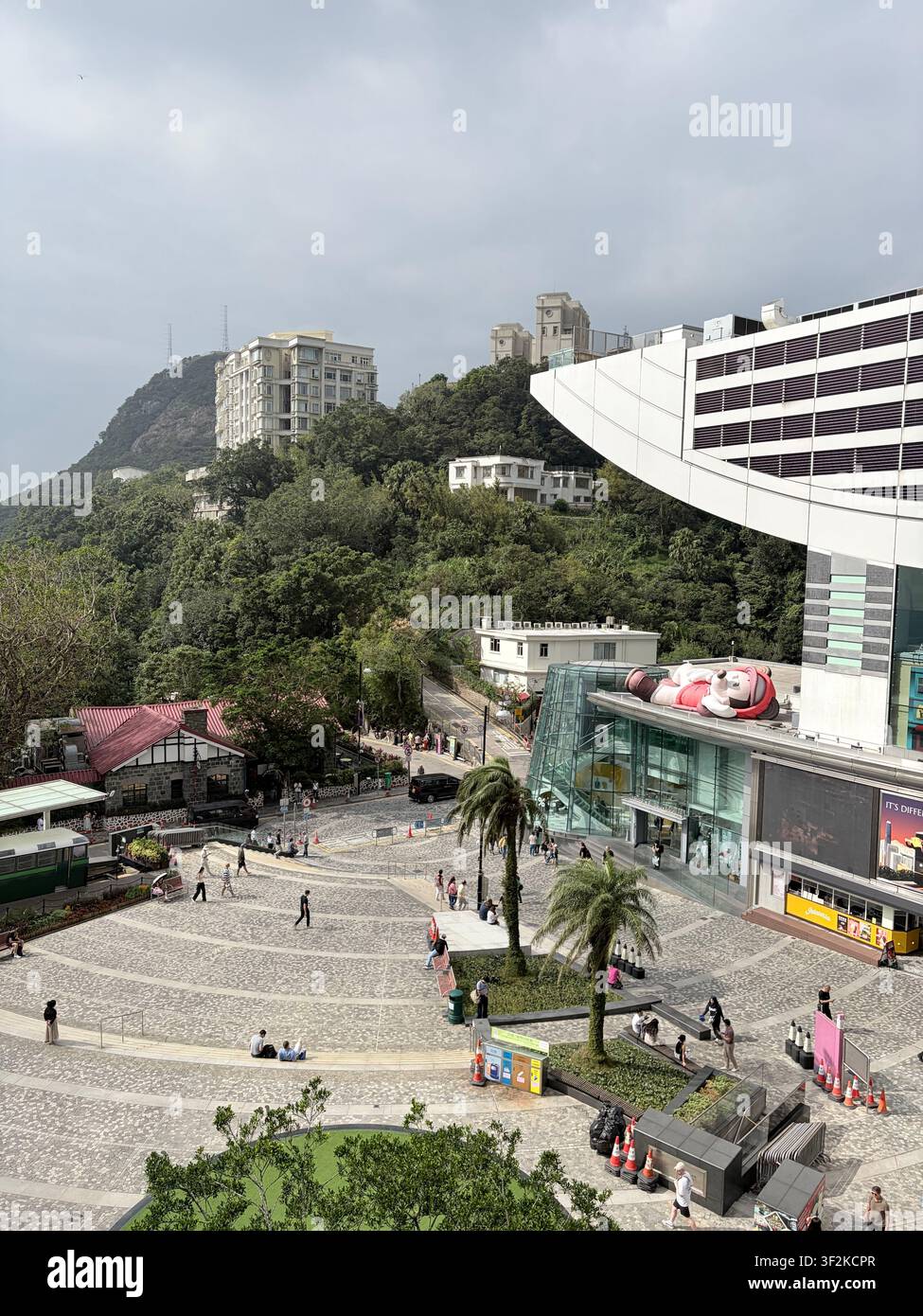 31 ottobre 2025, Hong Kong, Cina – Piazza commerciale della torre Victoria Peak con figura di Topolino, palme e turisti su una passeggiata lastricata. - Immagine stock catturata con smartphone