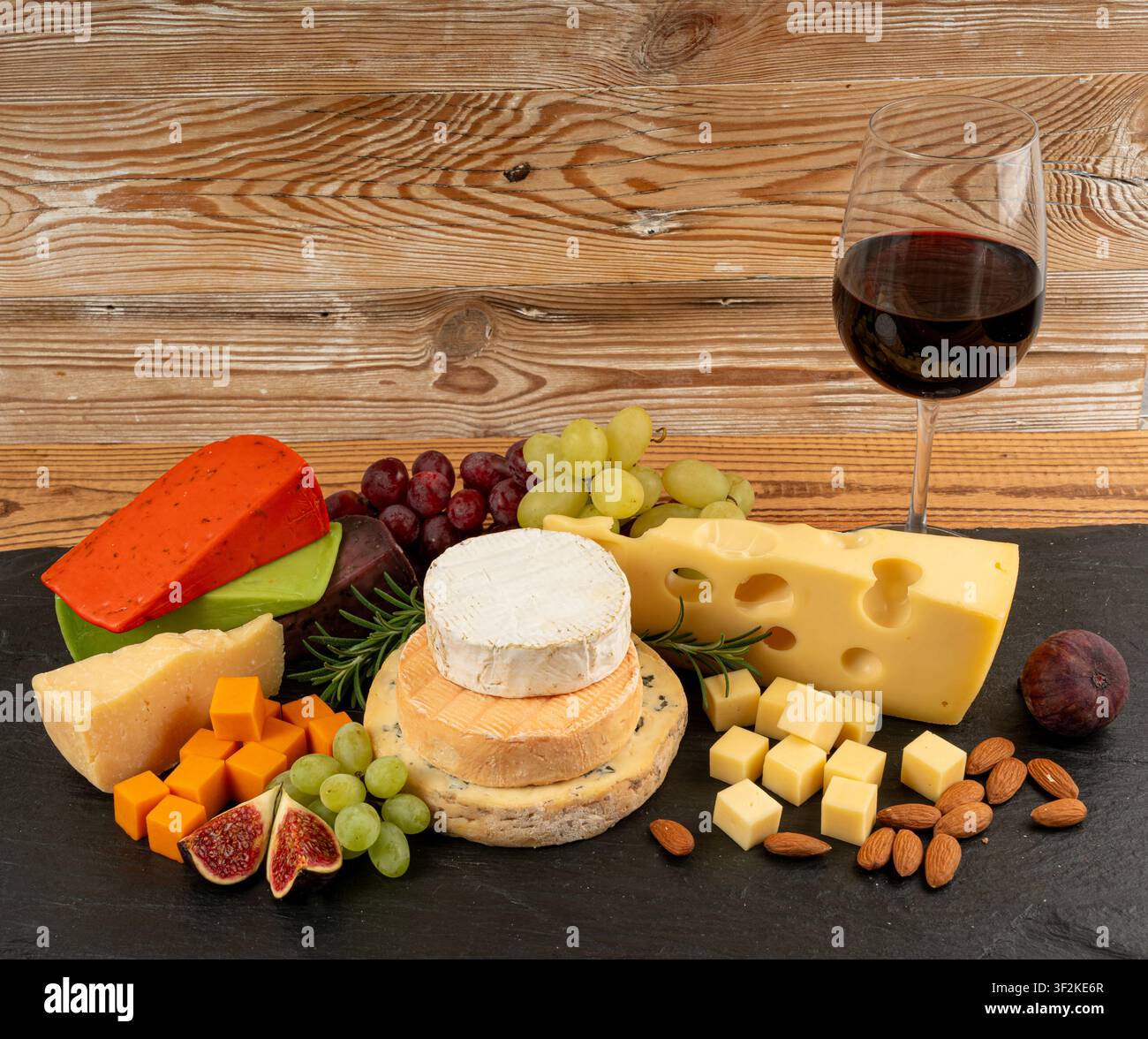 Piatto di formaggi vari colorati, piatto di gorgonzola giallo, bianco e blu con bicchiere di vino rosso, tagliere di formaggi, prodotti caseari tritati assortiti, m Foto Stock