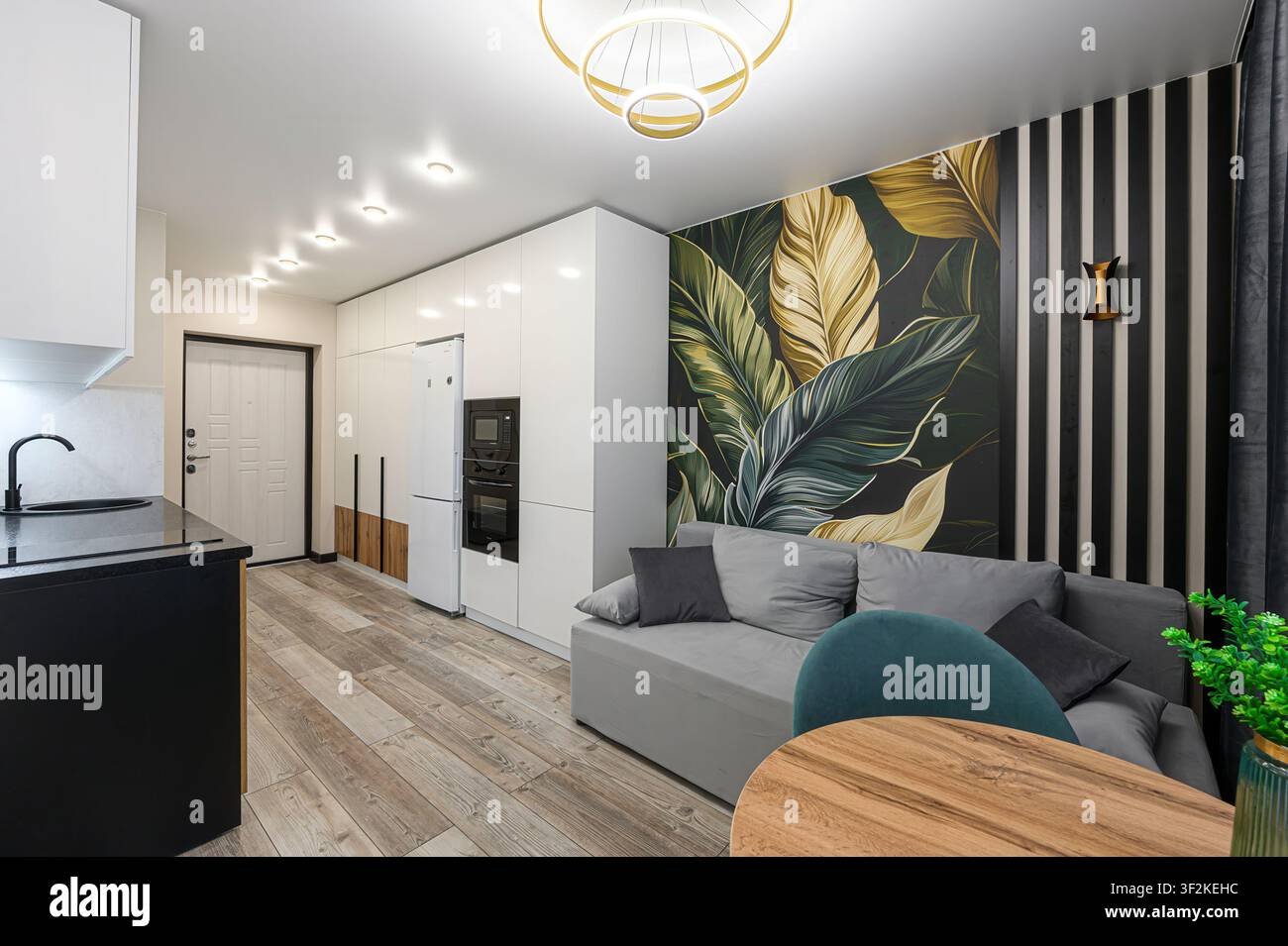 interno di appartamento moderno con un divano grigio, carta da parati tropicale, armadi bianchi eleganti e accenti di legno Foto Stock
