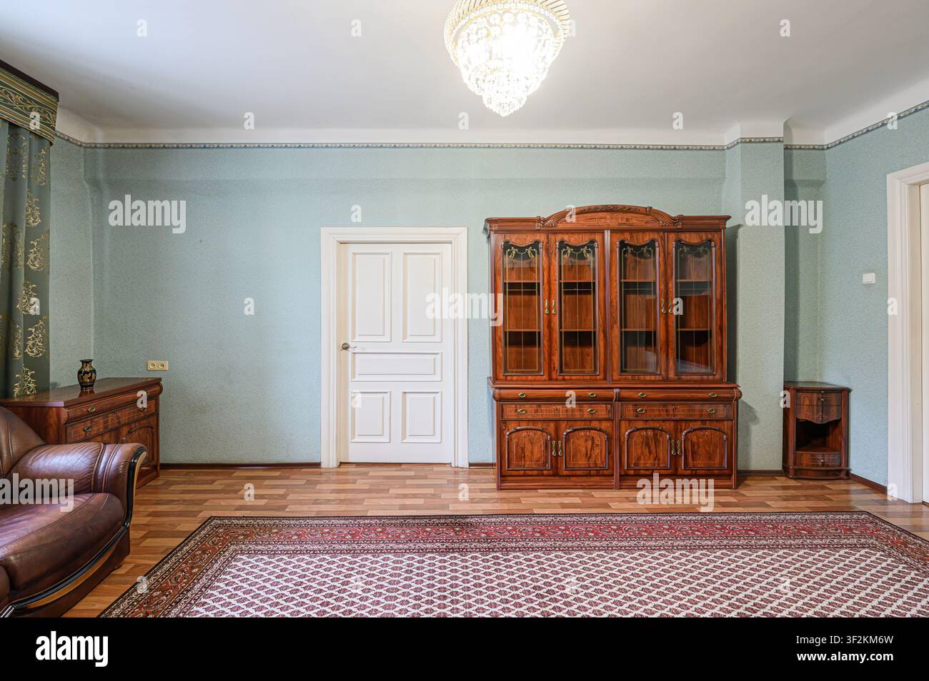 sala da pranzo classica con un armadio di legno, divano in pelle, tappeto a motivi e un lampadario di cristallo Foto Stock