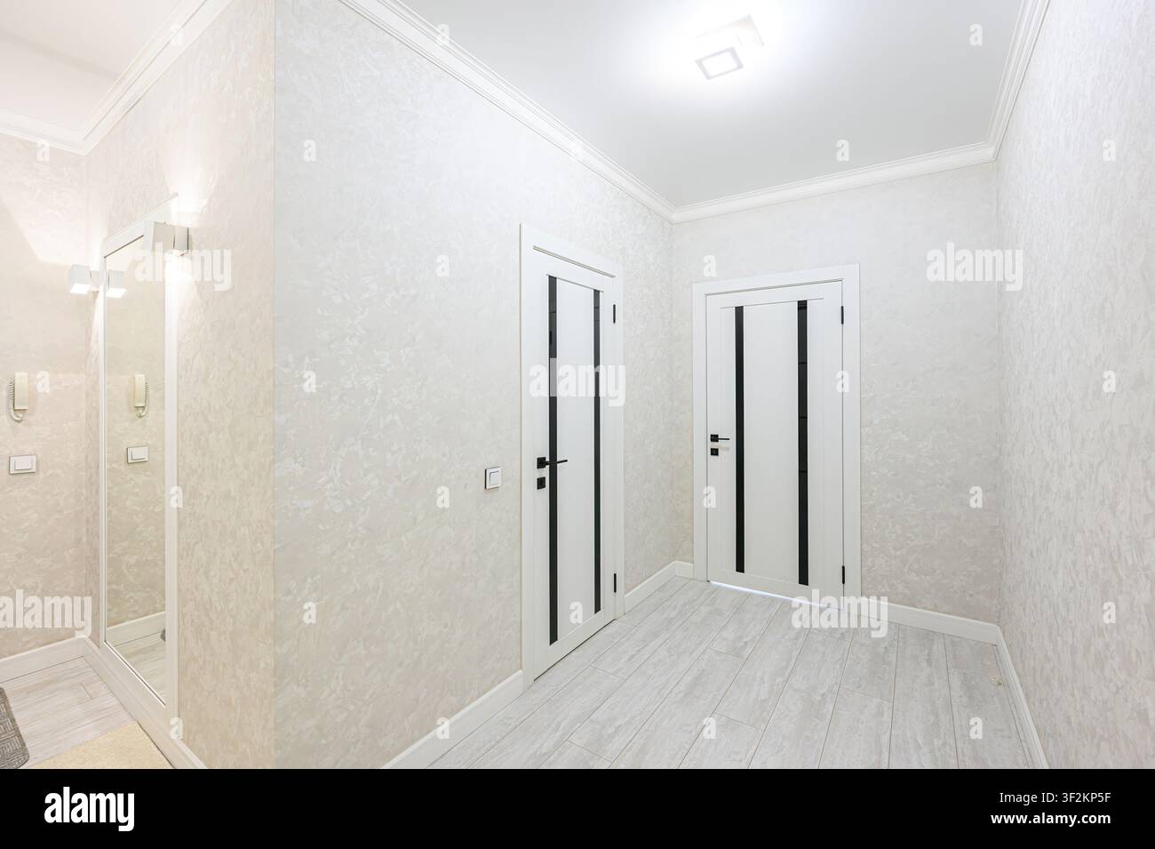 corridoio luminoso e moderno con carta da parati testurizzata, porte bianche con accenti neri e pavimenti in legno chiaro. Estetica pulita e minimalista Foto Stock
