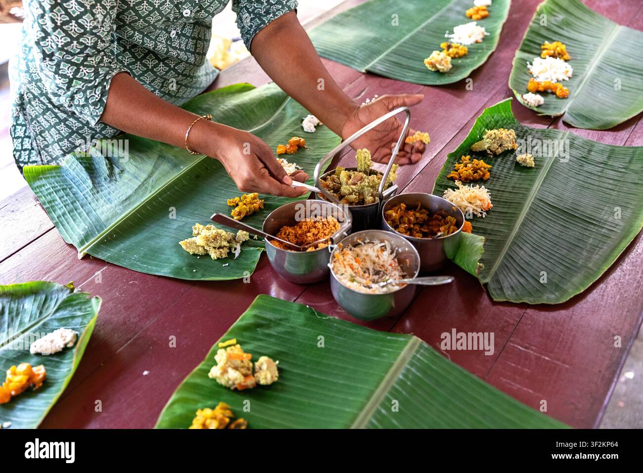 Donna del posto che serve un pranzo tradizionale indiano su foglie di banano in un alloggio a Munroe Island nelle backwaters del Kerala, India. Foto Stock