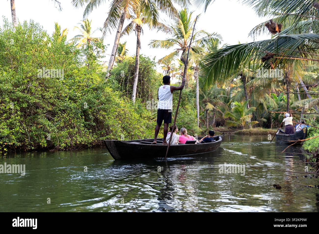 Turisti su barche di legno tradizionali che esplorano stretti canali d'acqua sull'isola di Munroe nelle backwaters del Kerala, in India, circondati da una lussureggiante vegetazione tropicale. Foto Stock