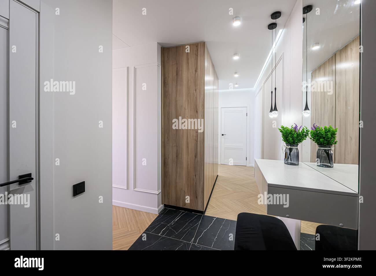 Corridoio moderno con accenti in legno, piastrelle di marmo nero, illuminazione elegante, un tavolo console minimalista e uno specchio a figura intera Foto Stock