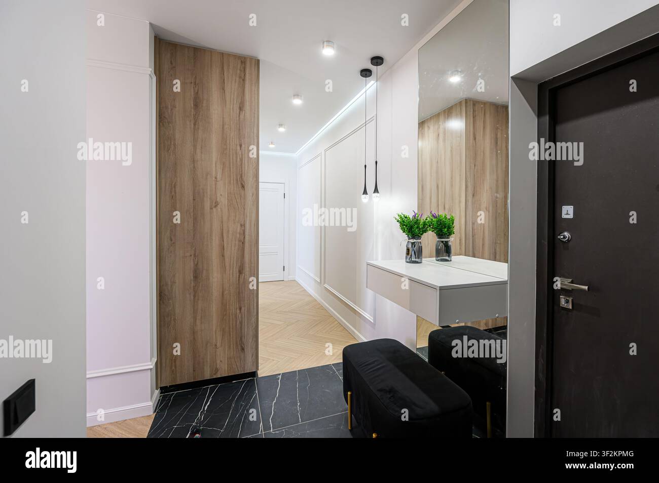 Corridoio moderno con accenti in legno, piastrelle di marmo nero, illuminazione elegante, un tavolo console minimalista e uno specchio a figura intera Foto Stock