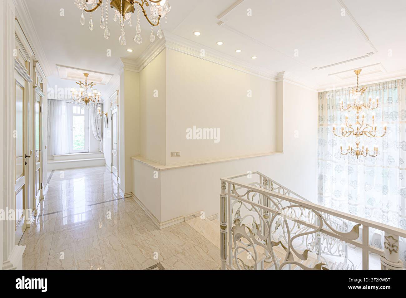 Interno elegante con pavimenti in marmo, pareti bianche, ringhiere decorative e lampadari di cristallo. Lo spazio emana lusso e sofisticazione Foto Stock